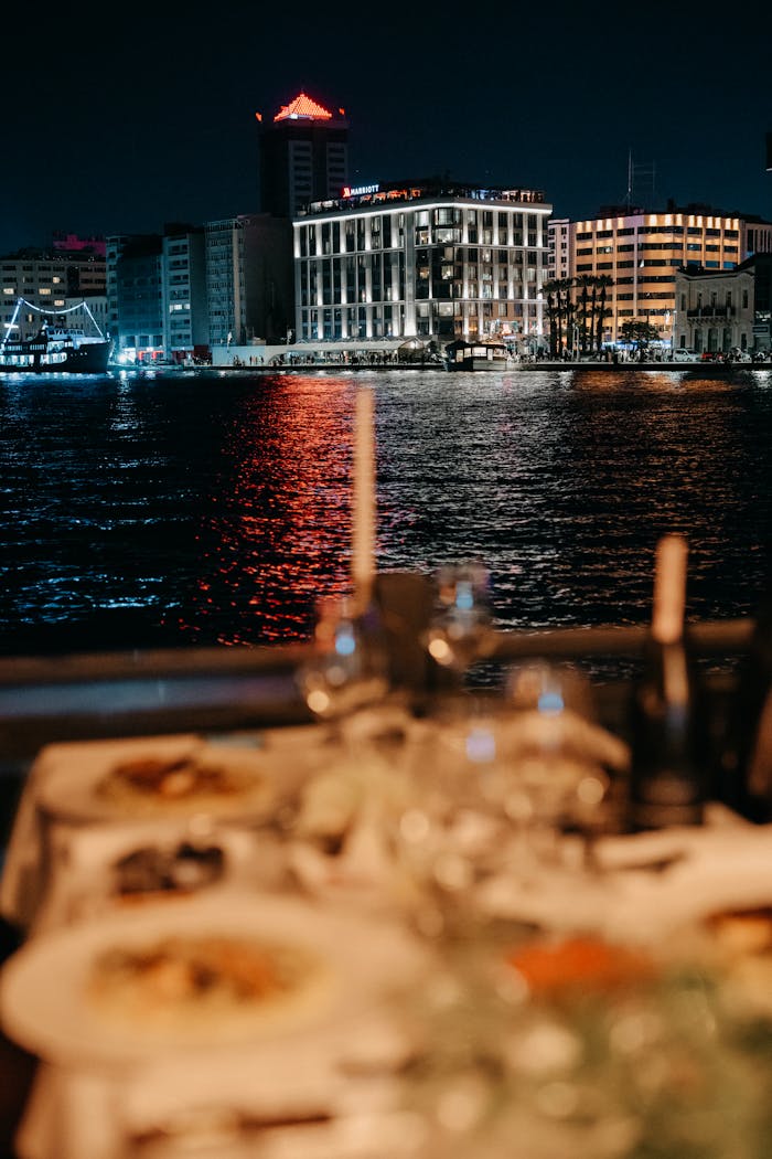 Elegant riverside dinner setup overlooking city lights and reflections on water at night.